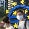 Dos personas con mascarillas faciales pasan frente a un gran símbolo del euro situado junto a la sede de Banco Central Europeo, el 24 de abril de 2020 en la ciudad alemana de Fráncfort