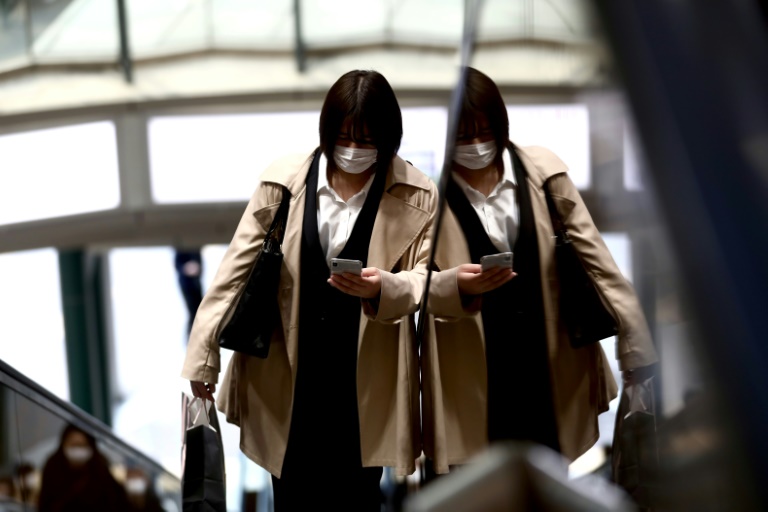 Una mujer con mascarilla mira su teléfono móvil mientras sube por una escalera mecánica de unos grandes almacenes de Tokio el 7 de abril de 2020.
