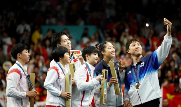 El medallista de bronce Lim Jong-hoon de Corea del Sur se toma un selfi con Shin Yu-bin de Corea del Sur y los medallistas de oro Chuqin Wang y Yingsha Sun de China, pero también con los medallistas de plata Ri Jong-sik y Kim Kum-yong de Corea del Norte, en el podio, este 30 de julio de 2024 en París. REUTERS - Kim Hong-Ji