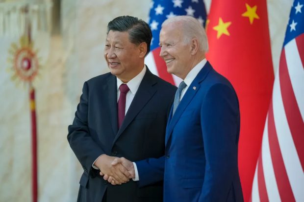 Joe Biden y Xi Jinping se apretan de manos mientras sonrien. Atrás de ellos las banderas de China y Estados Unidos