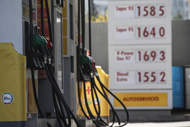 Mangueras de gasolina en una bencinera. Atrás difuminado se ven los precios de los combustibles.