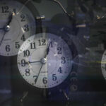 Tres relojes despertadores analógicos negros con reflejos sobre cristal y fondo oscuro.