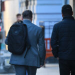 Desempleo sube a 8,9%: Gobierno califa la cifra de "inaceptable" Dos hombres se ven caminando de espaldas. Uno viste traje gris y tiene una mochila en su hombro. El otro viste chaqueta negra.