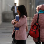 Gobierno, oposición y CUT chocan por alza del desempleo: sala cuna, salario mínimo y "demagogia" marcan disputa Una mujer de chaqueta rosa sujeta documentos contra su pecho en una calle urbana, junto a otra persona de espaldas con abrigo de invierno y mochila roja.