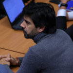 Joaquín Lavín León se ve de perfil sentado en una mesa de madera clara mientra ve al frente.