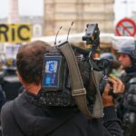 Un camarógrafo de prensa de espaldas, con una cámara profesional al hombro que muestra el logo de France 3, graba durante una protesta.