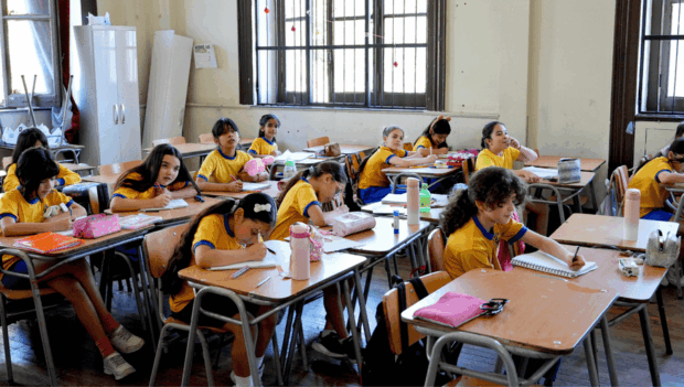 Alumnas sentadas en sus pupitres en un salón de clases. Todas visten ropa deportiva y polera amarilla.