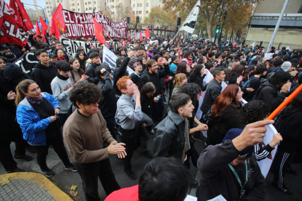 Multitud de estudiantes marcha entre banderas y carteles con consignas mientras gritan cánticos sobre educación.